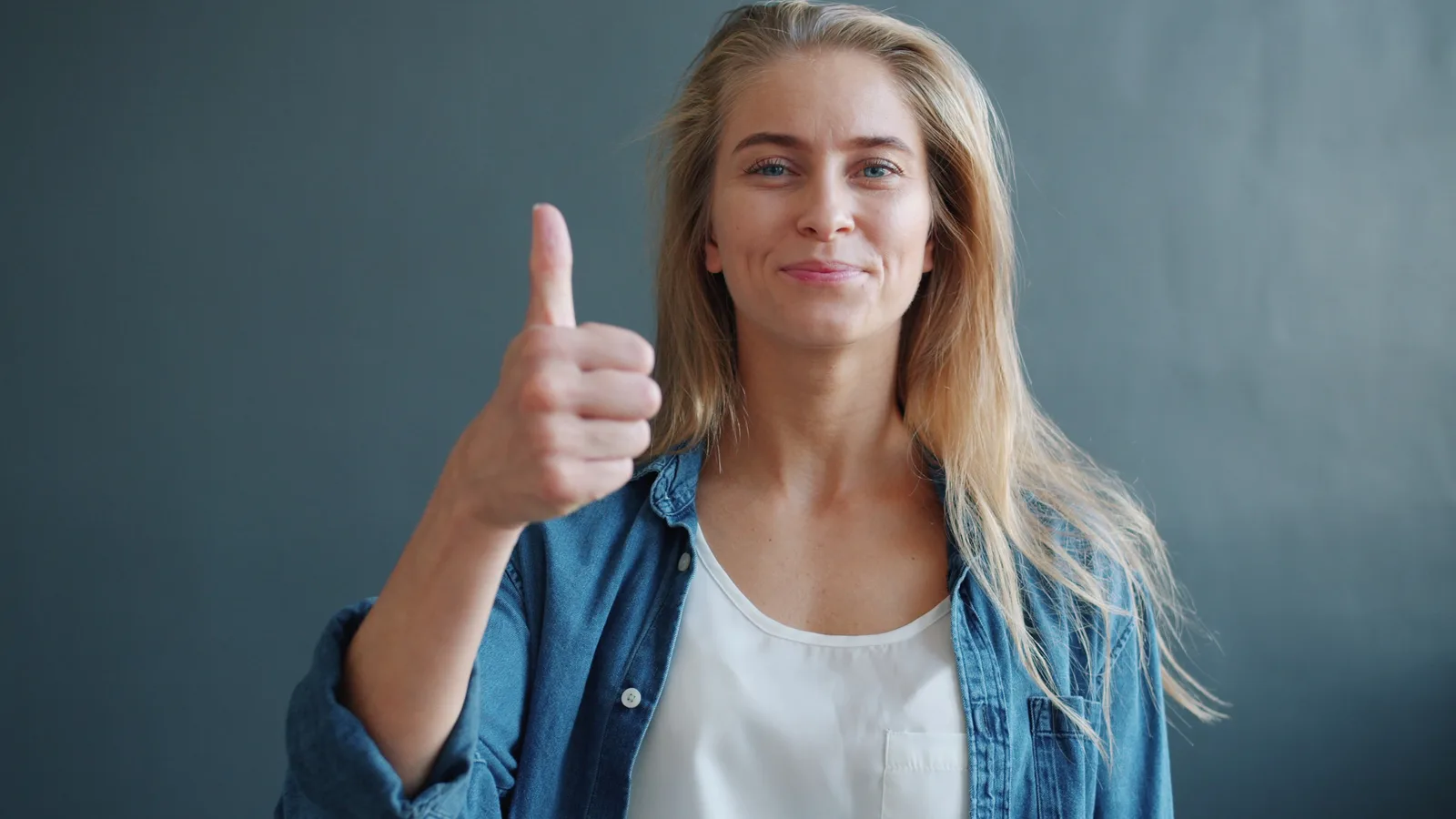 Portrait of a smiling woman giving a thumbs up against a neutral background.